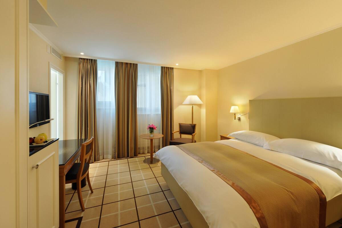 A hotel room with a bed, a desk with a chair, a television, and a lamp.