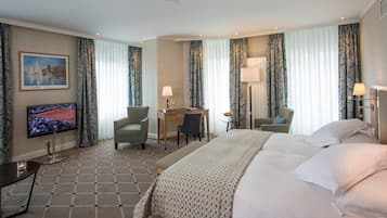 Een hotelkamer met een groot bed, een bureau met stoel, een televisie en een kleine tafel met lamp.