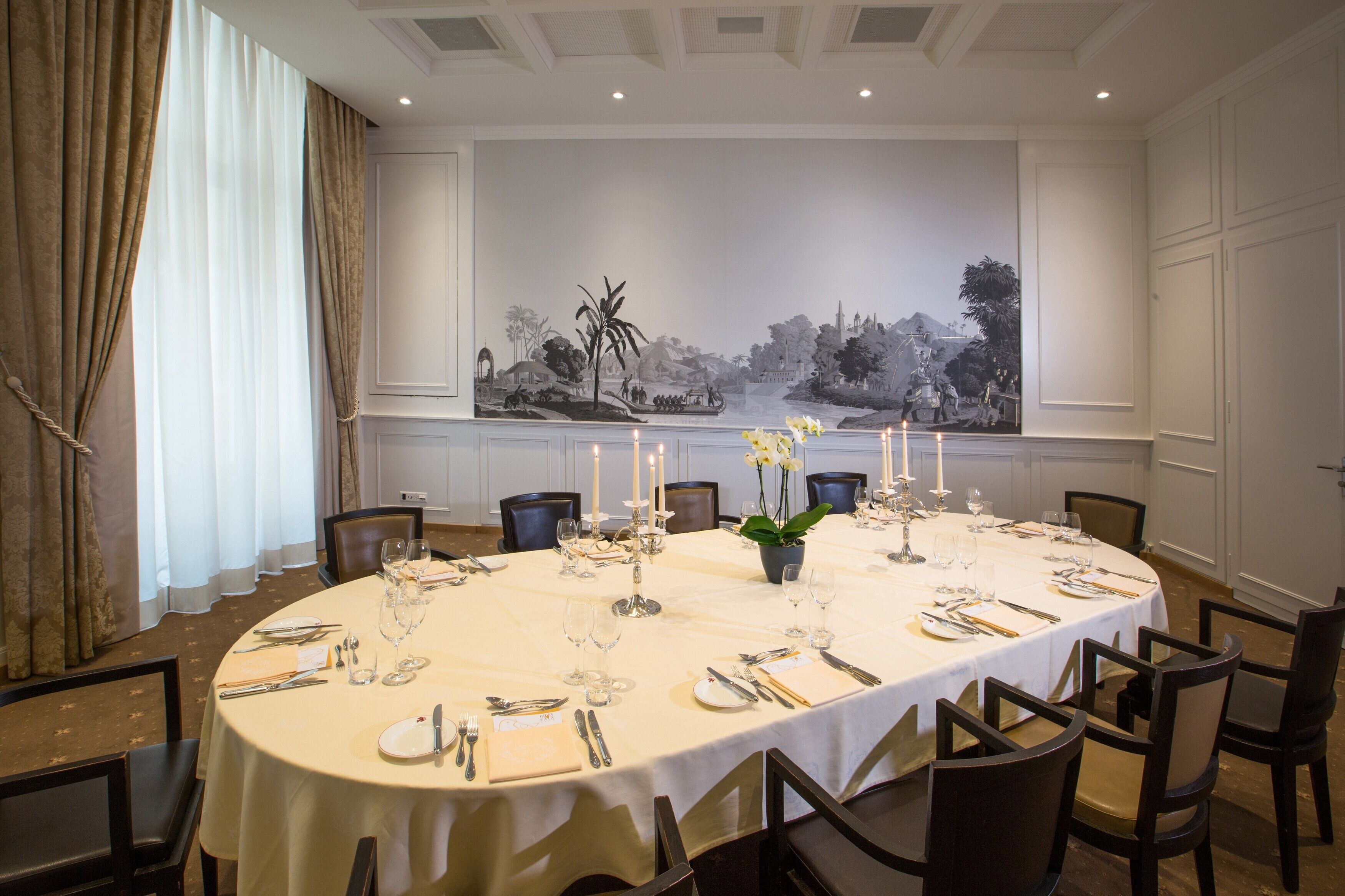 A dining room with a round table set for a meal, featuring candles, cutlery, and a vase of flowers.