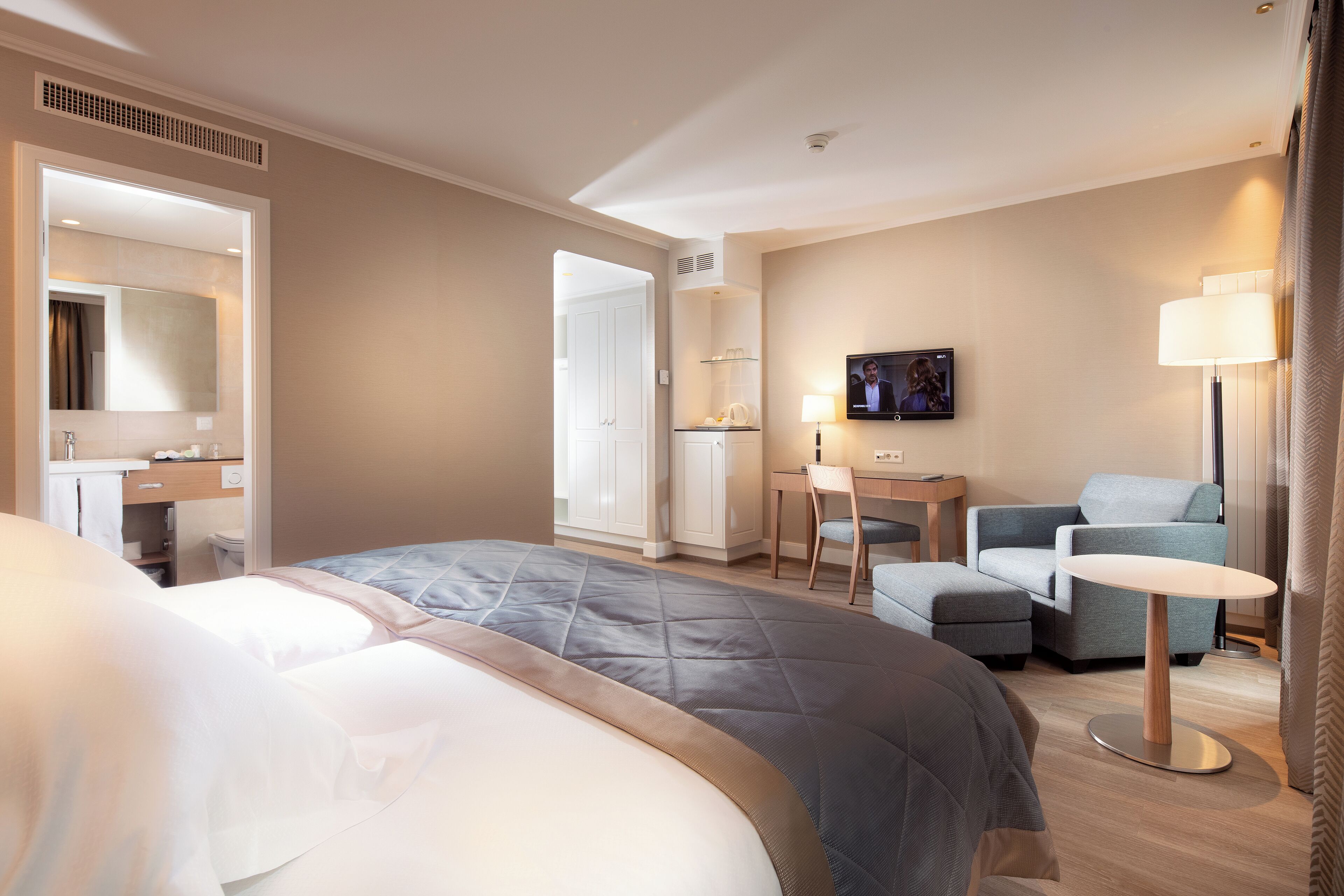 A hotel room with a large bed, a desk, a chair, and a television.