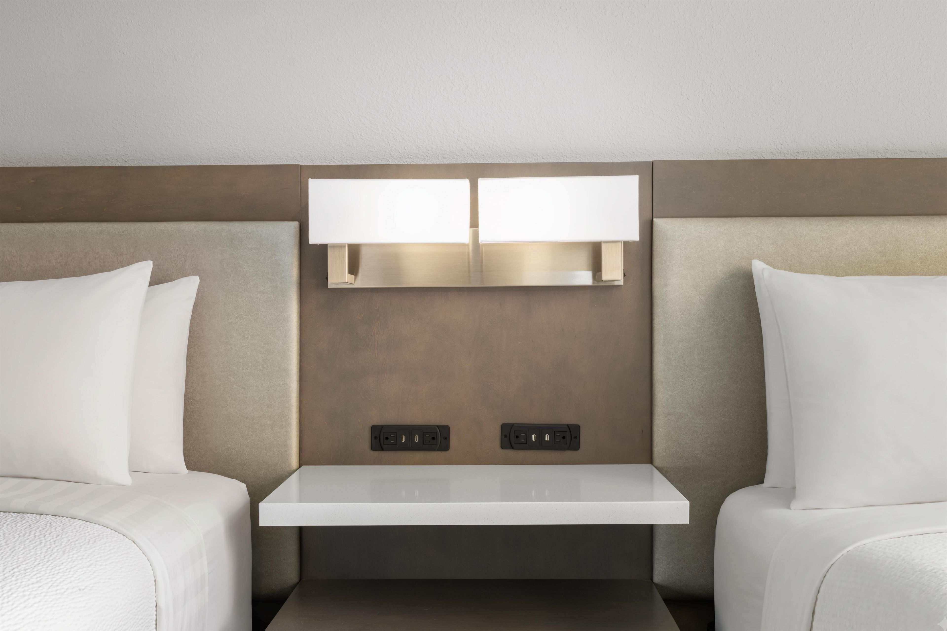 Une chambre d’hôtel avec deux lits, une table de chevet et un luminaire fixé au mur.