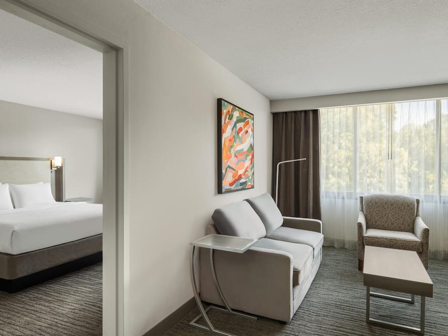 A hotel room with a bed, a sofa, a chair, a small table, and a window with curtains.
