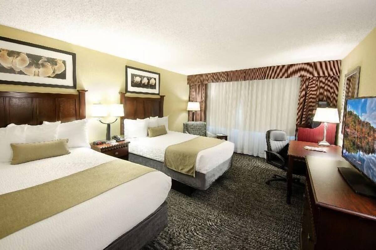 Une chambre d’hôtel avec deux lits, un bureau, une chaise, une télévision et des tableaux encadrés au mur.