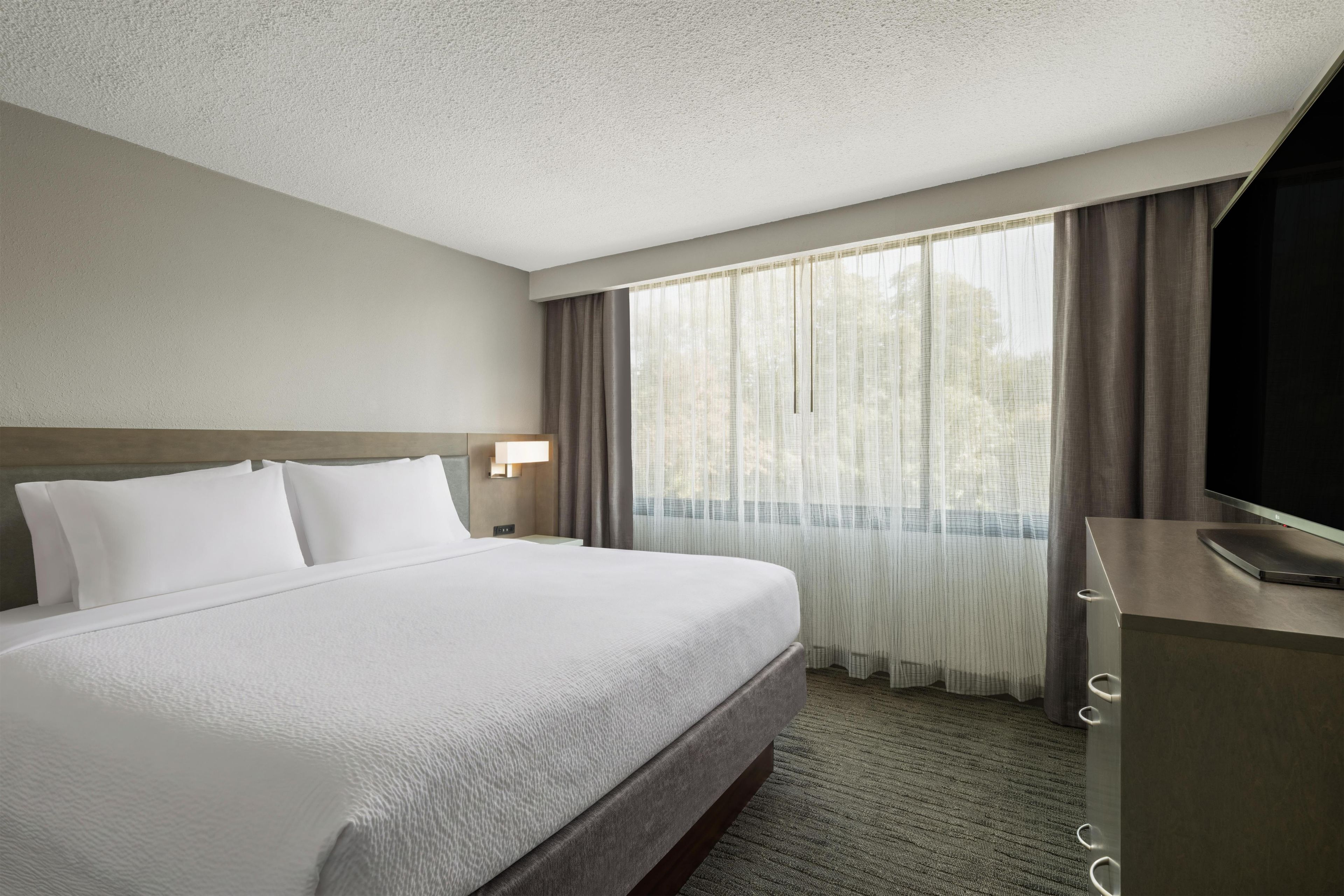 A hotel room with a large bed, a TV, a desk, and a window with curtains.