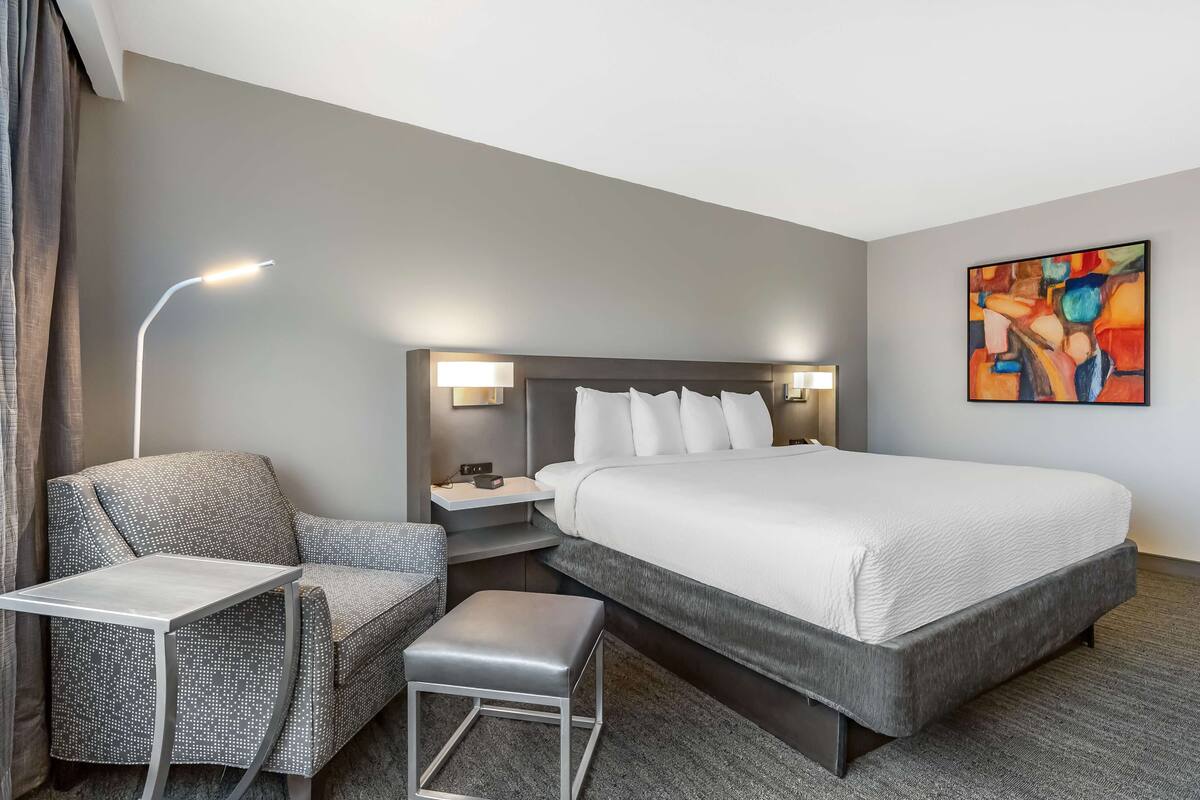 Une chambre d’hôtel avec un grand lit, une chaise, une petite table et une table de chevet avec une lampe.