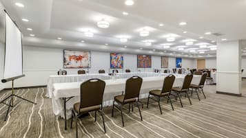 Uma sala de conferências com uma mesa comprida, cadeiras, uma tela de projetor e obras de arte nas paredes.