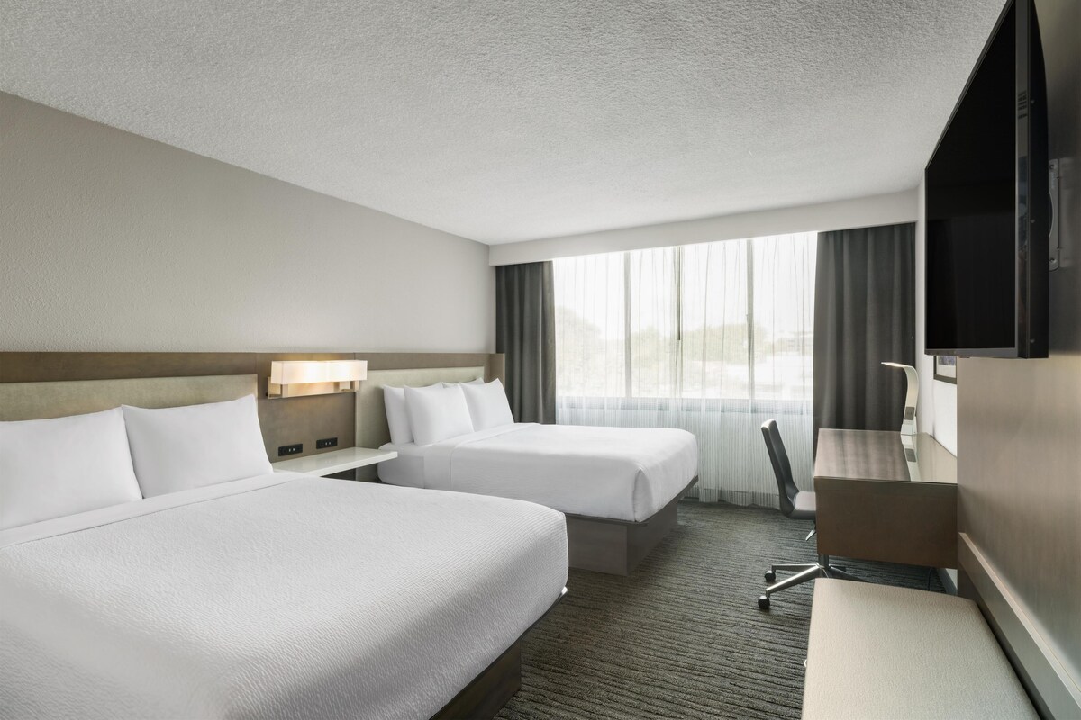 Une chambre d’hôtel avec deux lits, un bureau, une chaise et un téléviseur.