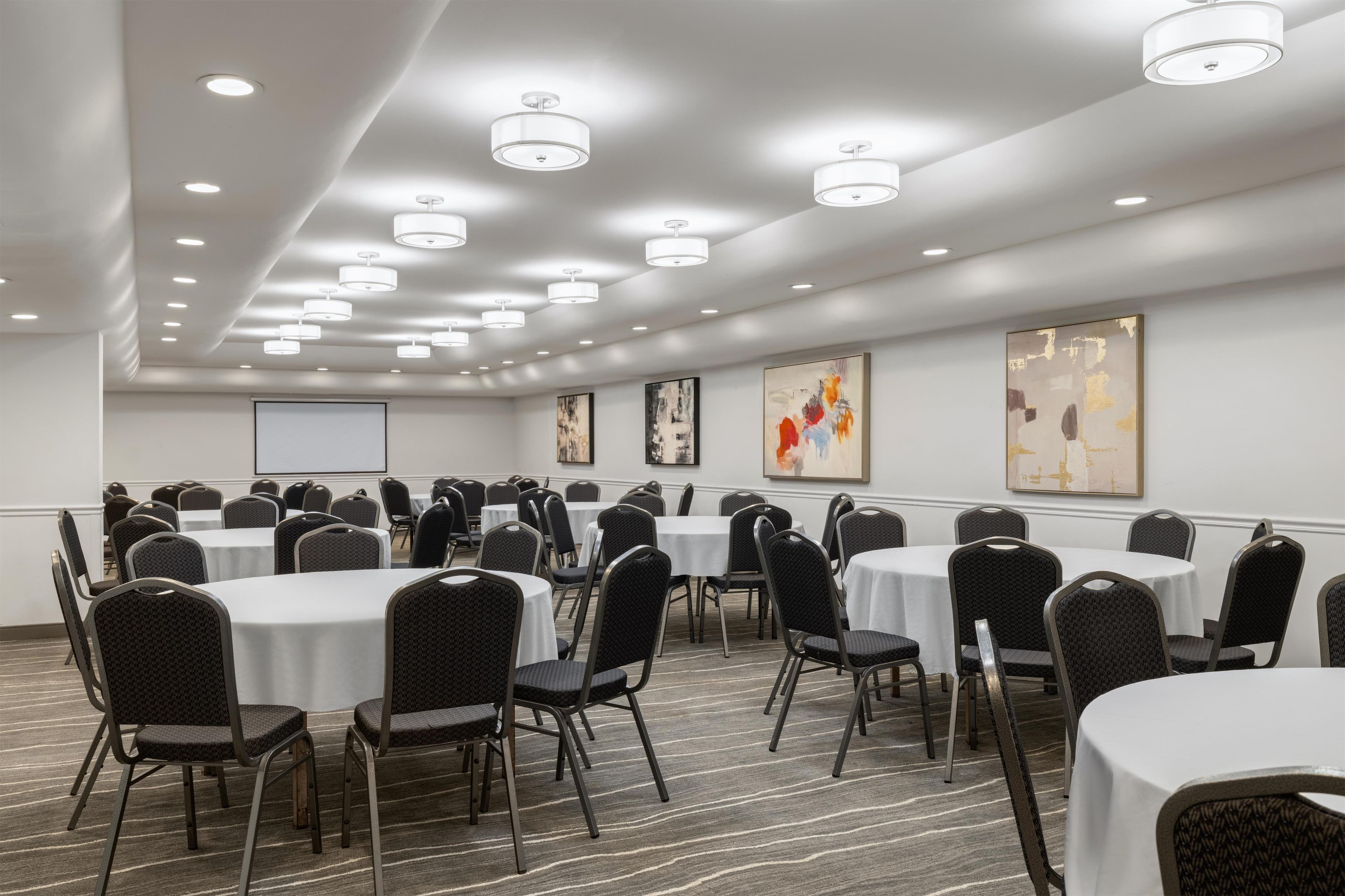 A conference room with round tables and chairs, recessed ceiling lights, and abstract art on the walls.