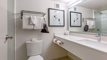 A modern bathroom with a toilet, sink, and glass shower enclosure. There are towels hanging on a rack, and a framed architectural drawing on the wall.