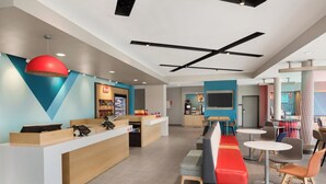 A modern hotel lobby with a reception desk, seating area, and a kitchen in the background.