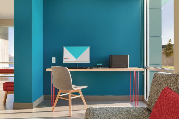 Un espacio de oficina moderno con una pared verde azulado, un escritorio con una computadora, una silla y un sofá con un cojín rojo.