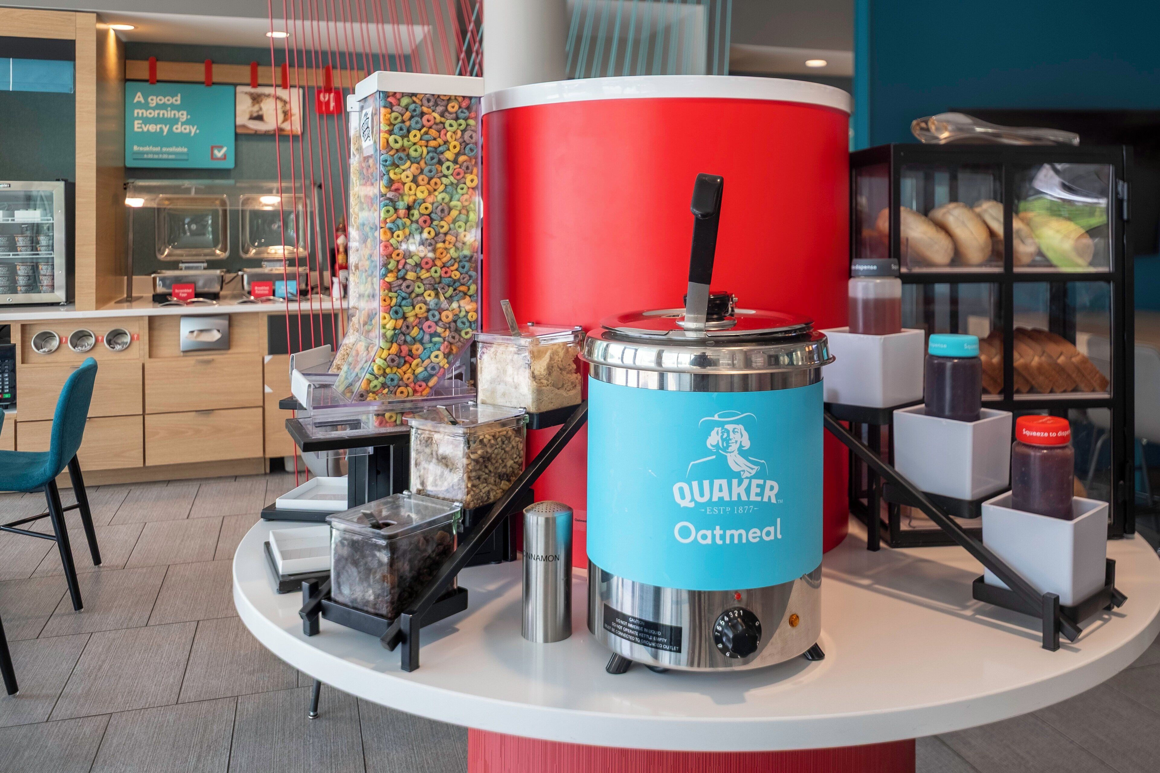 Un coin petit-déjeuner équipé d’une machine à café pour préparer du café à l’avoine Quaker, de distributeurs de céréales et d’une variété de produits de boulangerie.