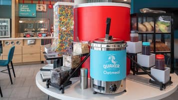 A breakfast station with a Quaker Oatmeal coffee maker, cereal dispensers, and a variety of baked goods.