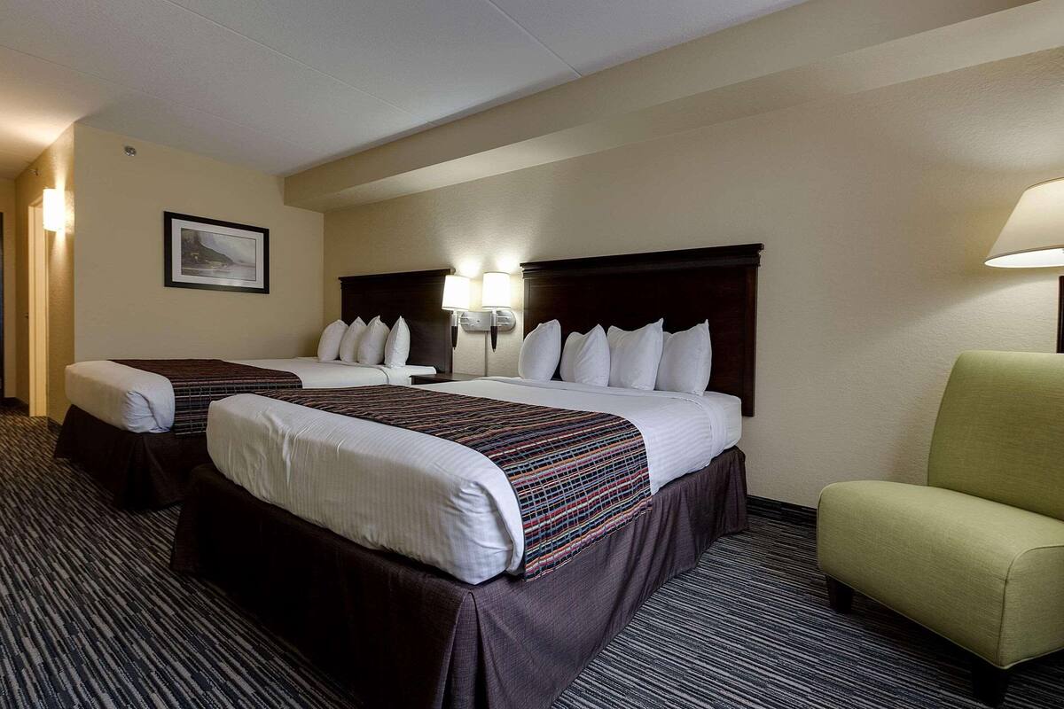 A hotel room with two beds, a large headboard, a green armchair, and a framed picture on the wall.