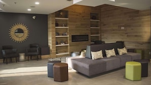 A modern living room with a grey sofa, black and green ottomans, and a wooden accent wall. - Country Inn & Suites by Radisson, Niagara Falls, ON (Niagara Falls)