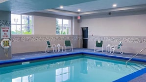 An indoor swimming pool with clear blue water, surrounded by white chairs and a tiled wall with a warning sign. - Country Inn & Suites by Radisson, Niagara Falls, ON (Niagara Falls)