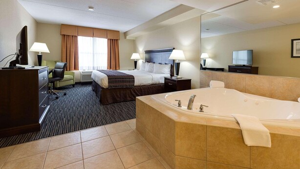 A hotel room with a large bed, a separate sitting area with a chair and desk, a bathroom with a bathtub, and a television. - Country Inn & Suites by Radisson, Niagara Falls, ON (Niagara Falls)