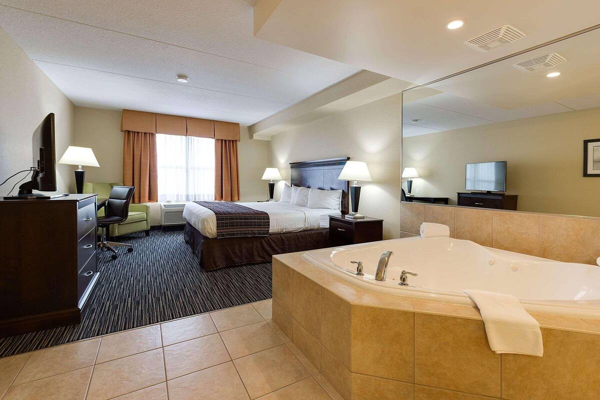 A hotel room with a large bed, a separate sitting area with a chair and desk, a bathroom with a bathtub, and a television.