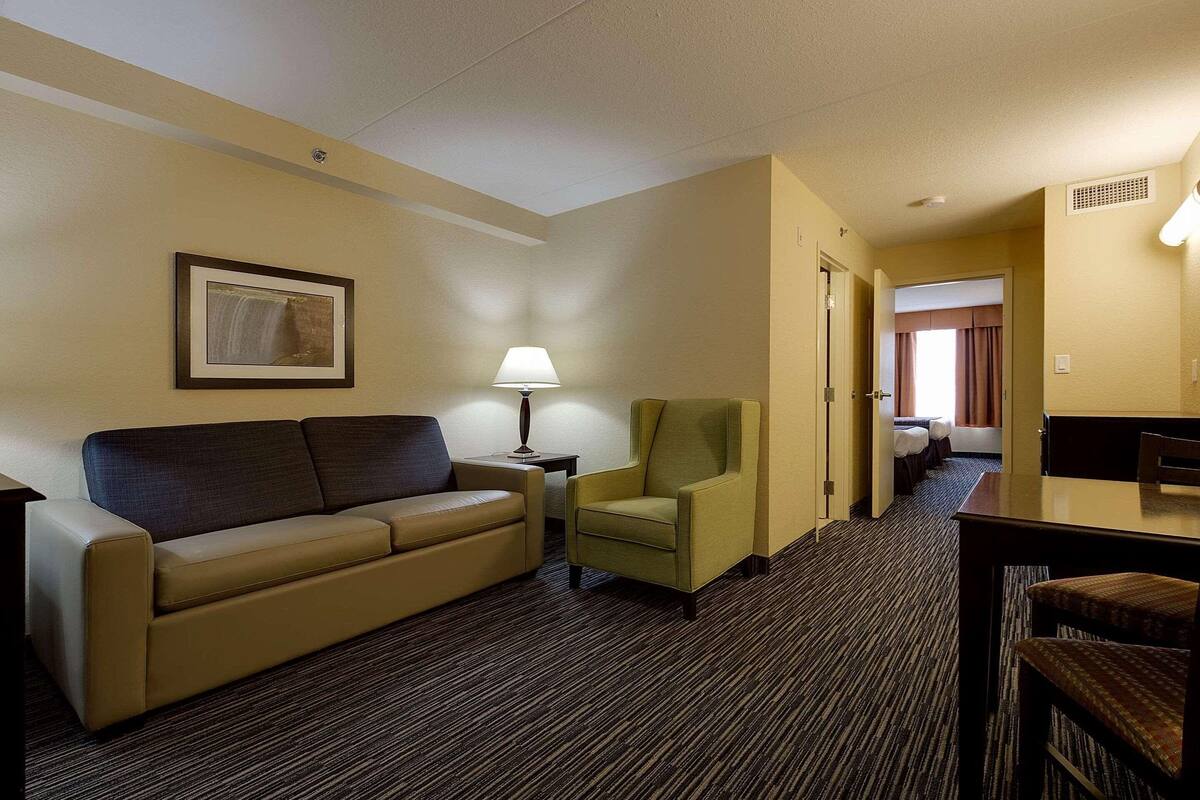 A hotel room with a sofa, armchair, lamp, and a framed picture on the wall.