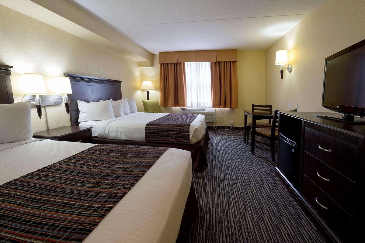 A hotel room with two beds, a desk, a television, and a dresser.