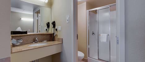 A bathroom with a sink, mirror, hairdryer, and a glass shower door.