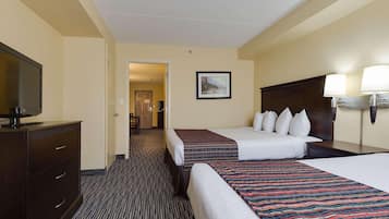 A hotel room with two beds, a TV on a dresser, and a hallway leading to another room.