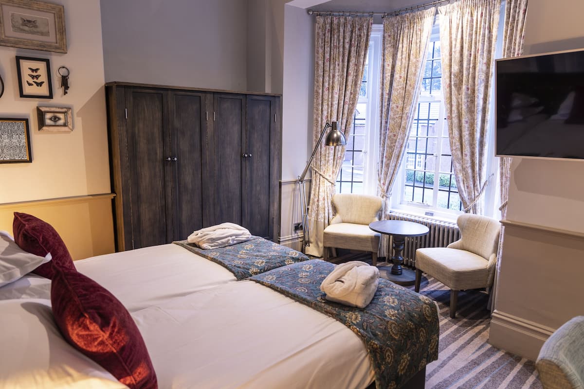 A hotel room with a large bed, two chairs, a TV, and a window with curtains.