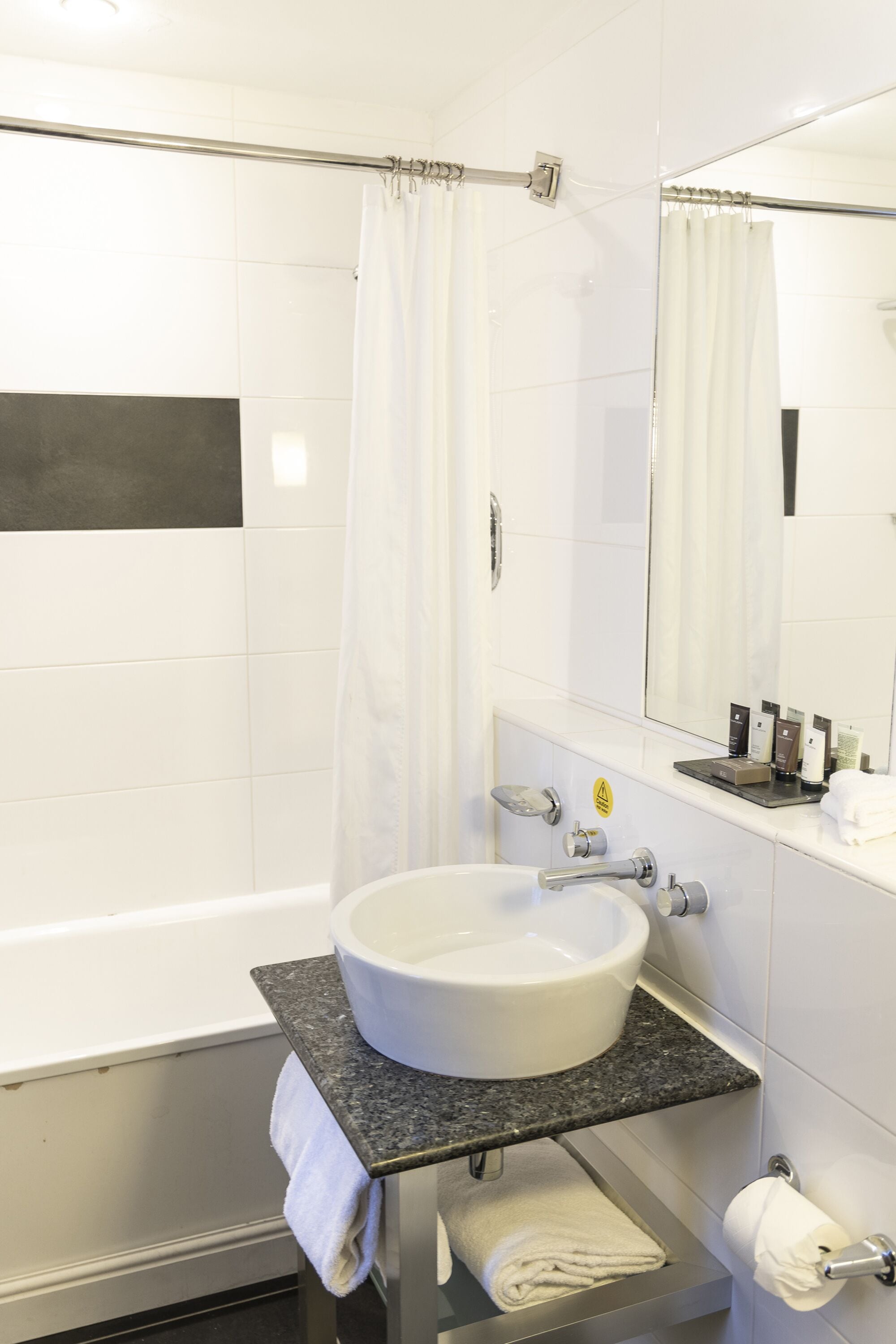 Een moderne badkamer met een wit bad, een wastafel met een marmeren blad, een handdoekhouder en een spiegel.