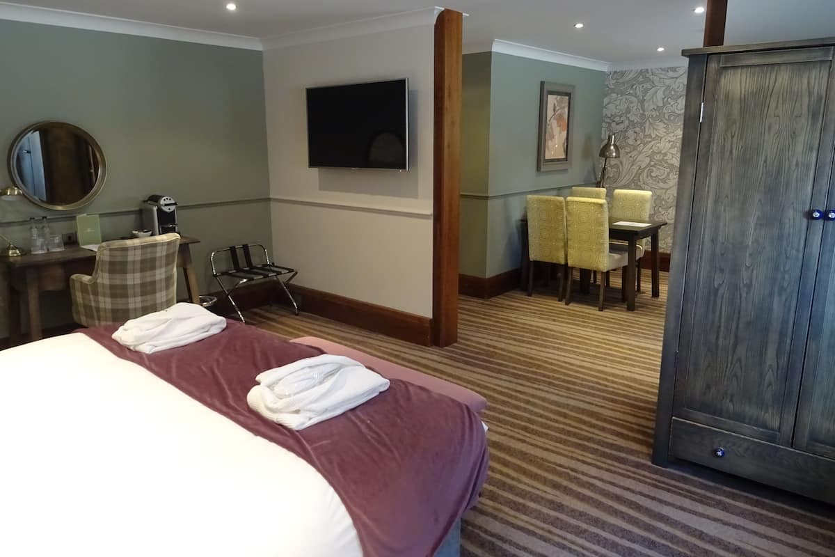 A hotel room with a large bed, a desk with a chair, a television, a wardrobe, and a dining area with chairs and a table.