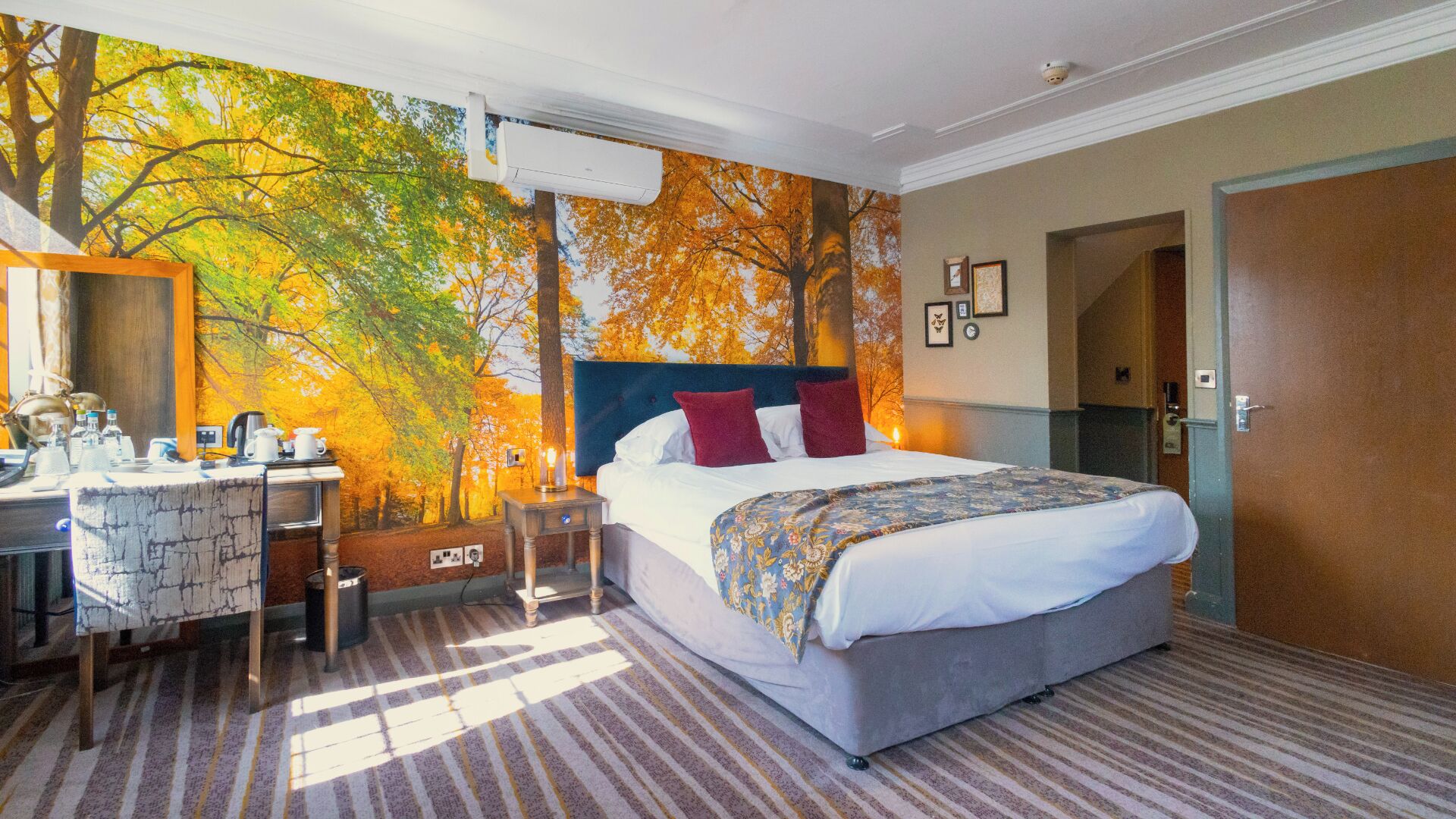 A hotel room with a bed, a desk, a chair, a mirror, and a wall mural.