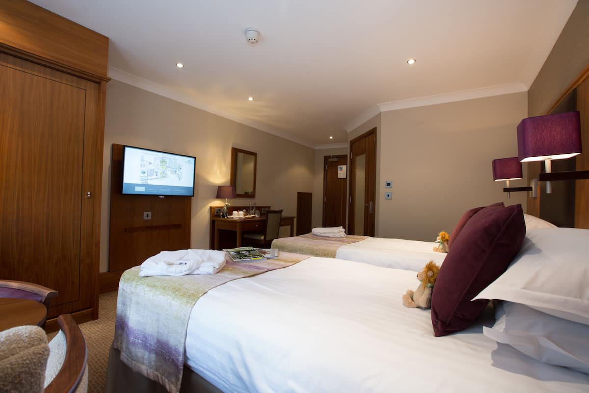 A hotel room with two beds, a desk, a television, and a wardrobe.