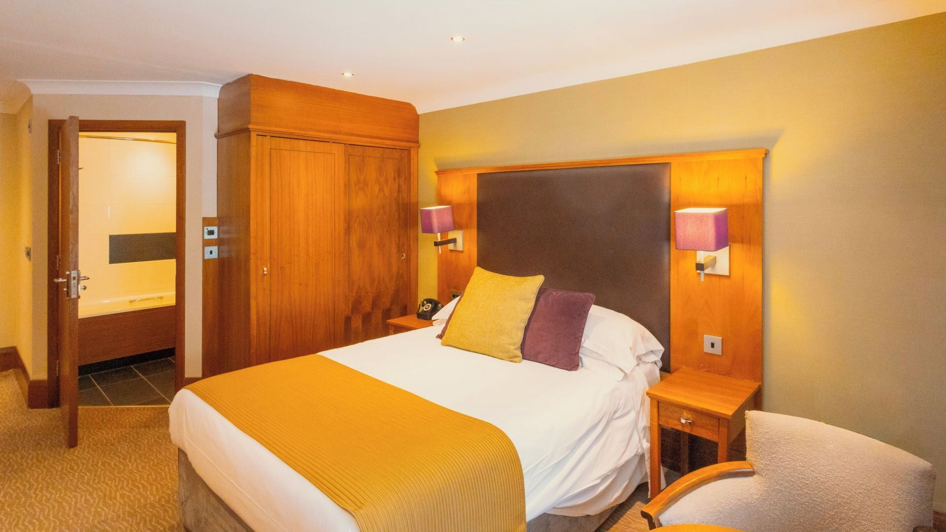 Habitación de hotel con una cama grande, armario de madera, lámparas de noche y una silla.