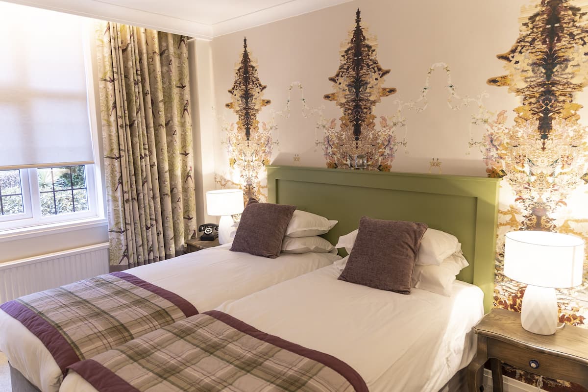 A double bed with a plaid bedspread, two pillows, a green headboard, and a nightstand with a lamp.