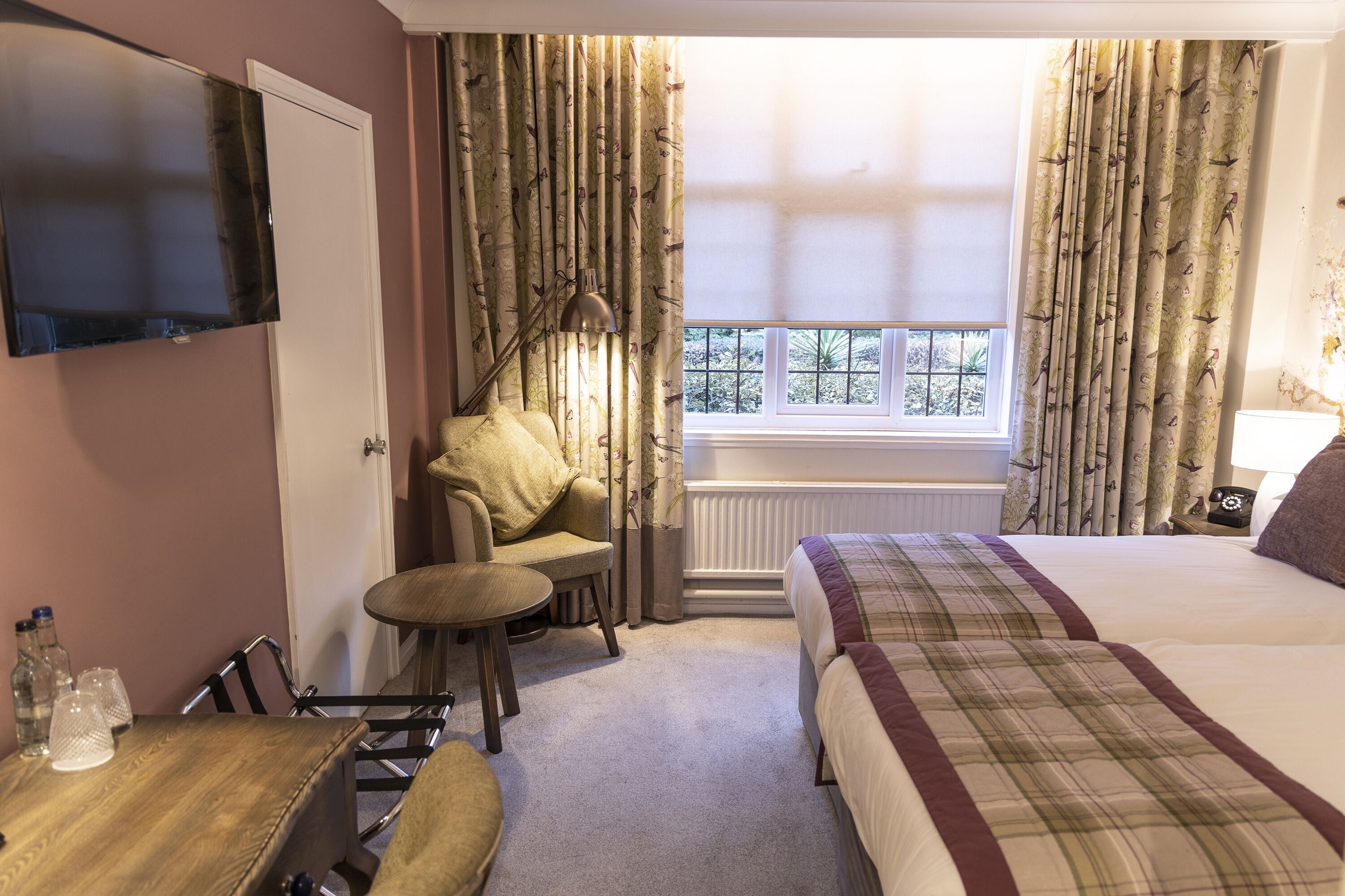 A hotel room with a bed, a chair, a table, a TV, and a window with curtains.
