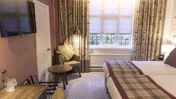 A hotel room with a bed, a chair, a table, a TV, and a window with curtains.
