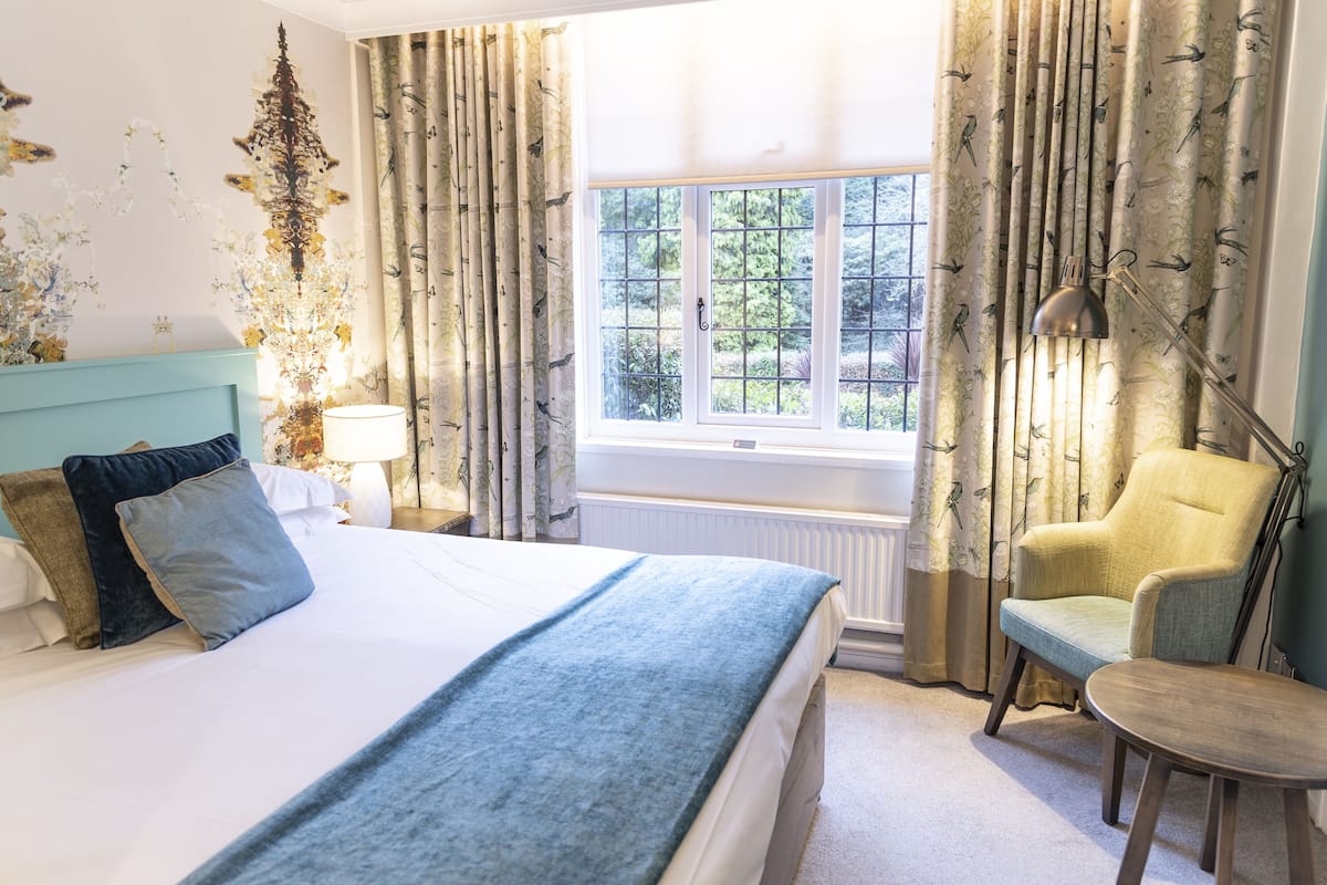 A neatly arranged bedroom with a bed, a chair, a table, and a window with curtains.