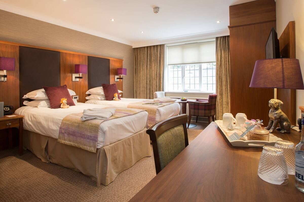 A hotel room with two beds, a desk, a chair, a TV, and a bathroom.