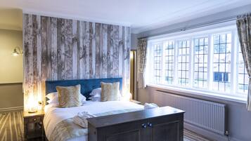 Un dormitorio con una cama grande, cabecera de madera, mesita de noche, cómoda y una ventana con cortinas.