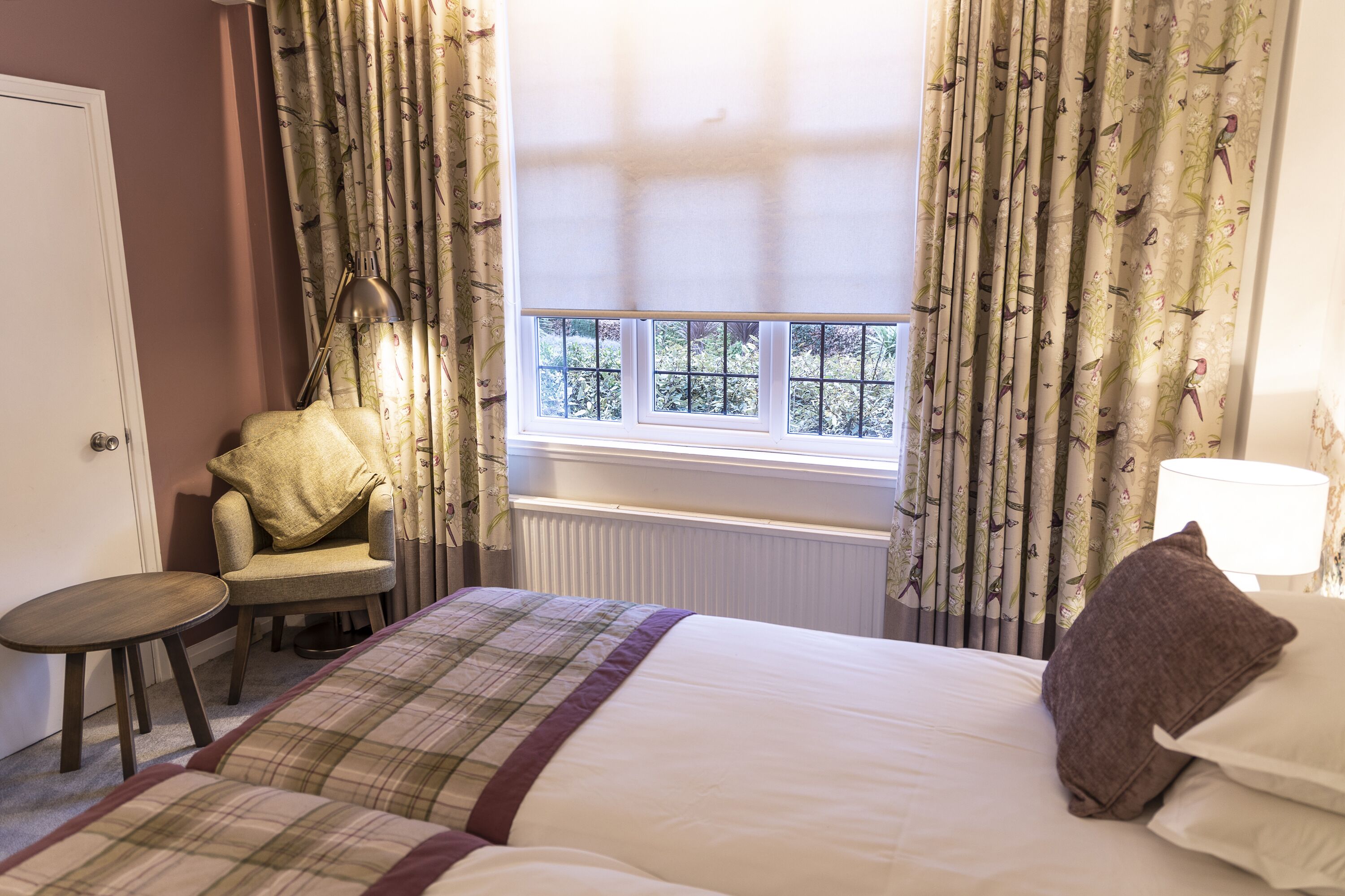 A hotel room with a bed, a chair, a small table, and a window with curtains.