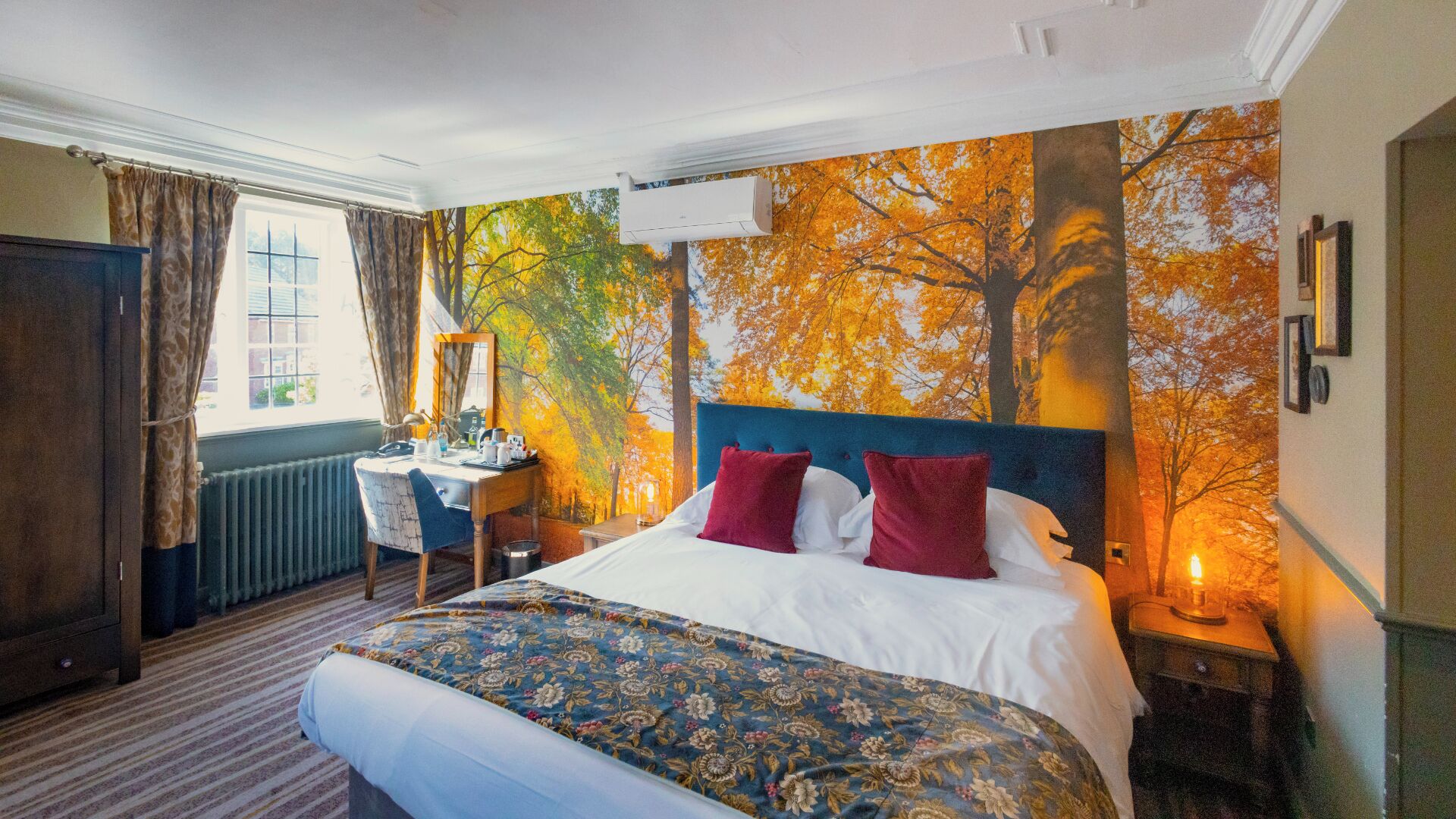 Habitación de hotel con una cama grande, un escritorio y vistas de árboles otoñales a través de una ventana.
