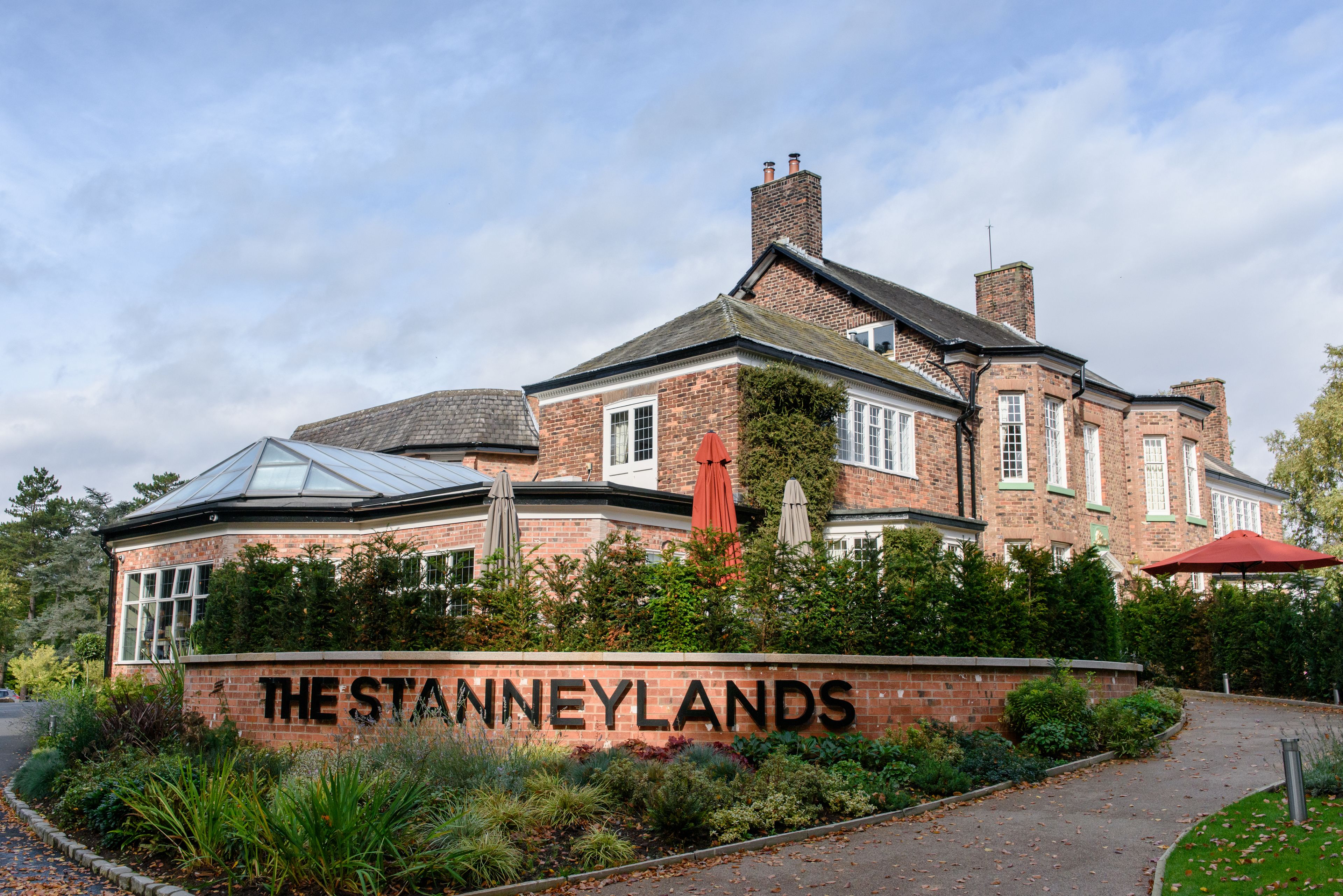 A brick building with a sign reading "THE STANNEYLANDS" surrounded by greenery.