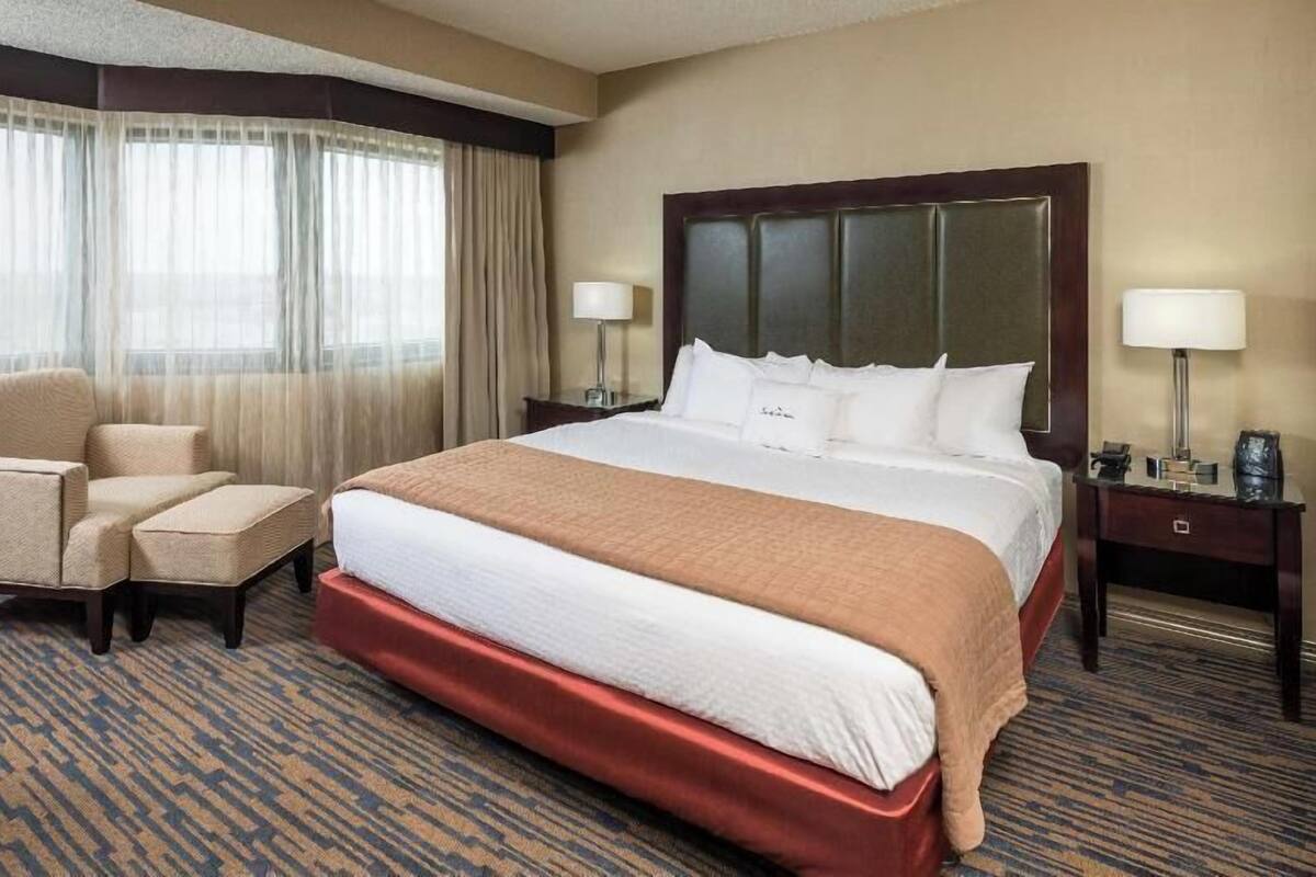 A hotel room with a large bed, a chair, a nightstand, and a lamp.