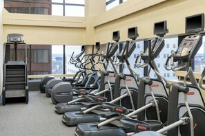 Une salle de sport équipée de plusieurs tapis de course, de vélos elliptiques et d’un appareil de marche en escalier, avec de grandes fenêtres donnant sur la ville.