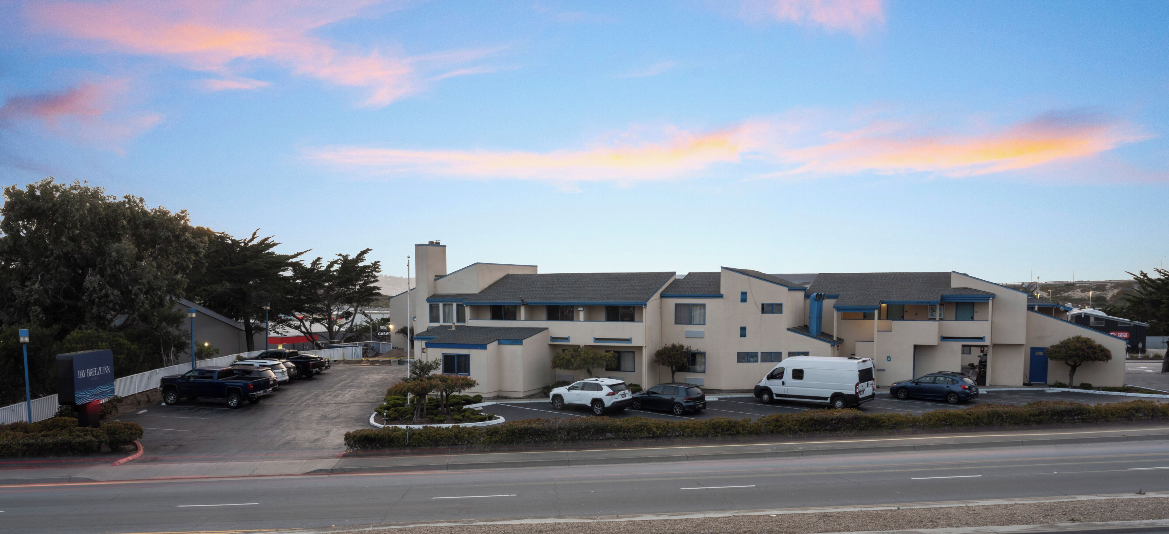 A multi-story motel with a parking lot, a signboard, and a clear sky.
