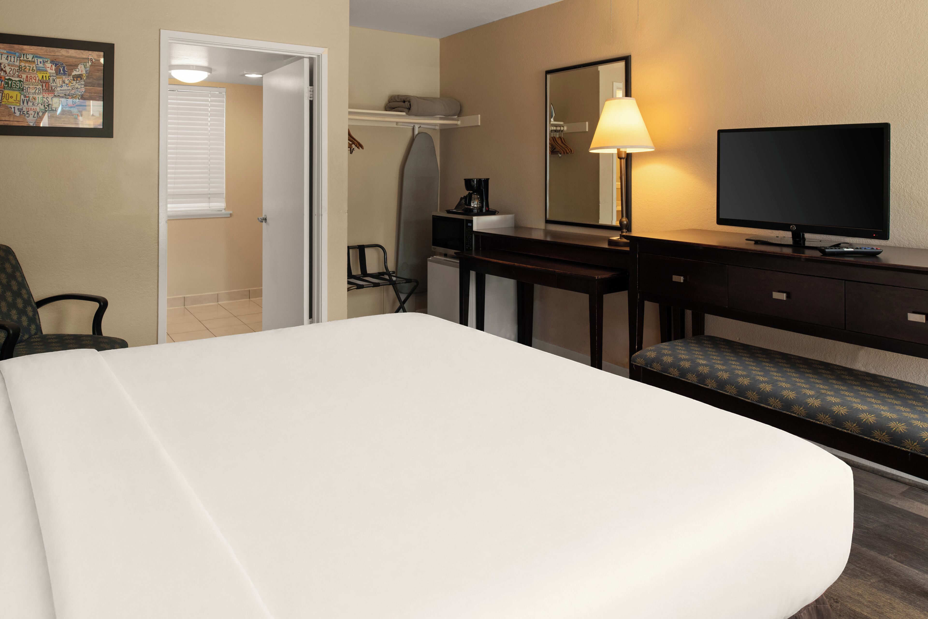 Habitación de hotel con cama, escritorio con computadora, televisor, banca y puerta que da a un baño.