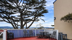 A deck with red flooring, striped white and blue railing, and outdoor furniture including chairs and a table.