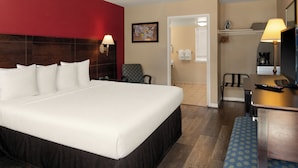 A hotel room with a large bed, a desk with a lamp, a chair, and a television.