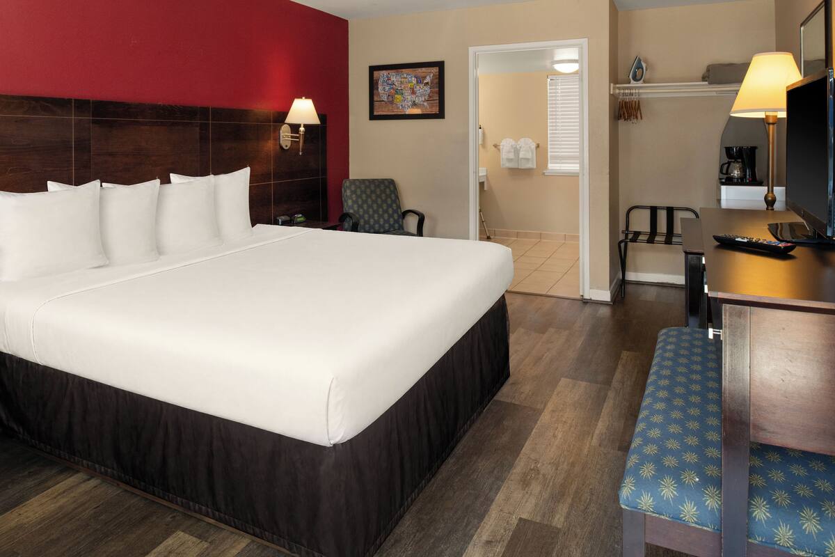 Una habitación de hotel con una cama grande, un escritorio con lámpara, una silla y un televisor.