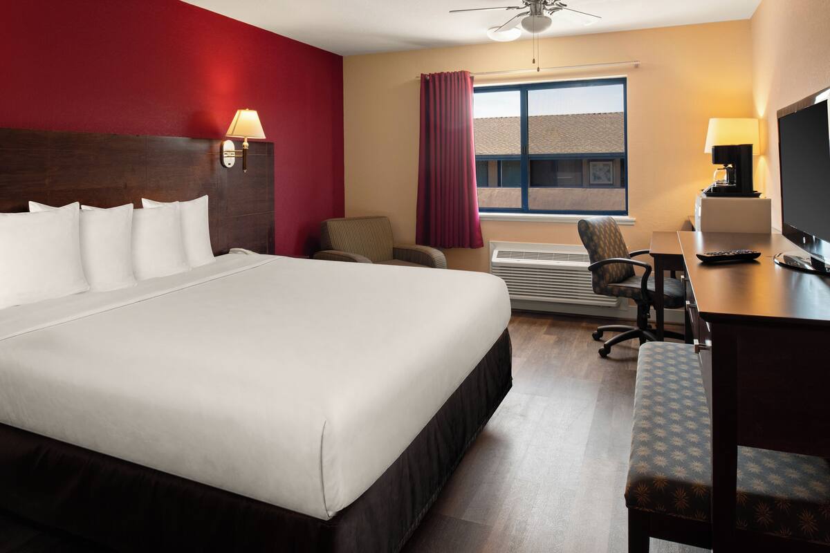 Habitación de hotel con una cama grande, un escritorio con computadora, una silla, televisor y ventana con cortinas.
