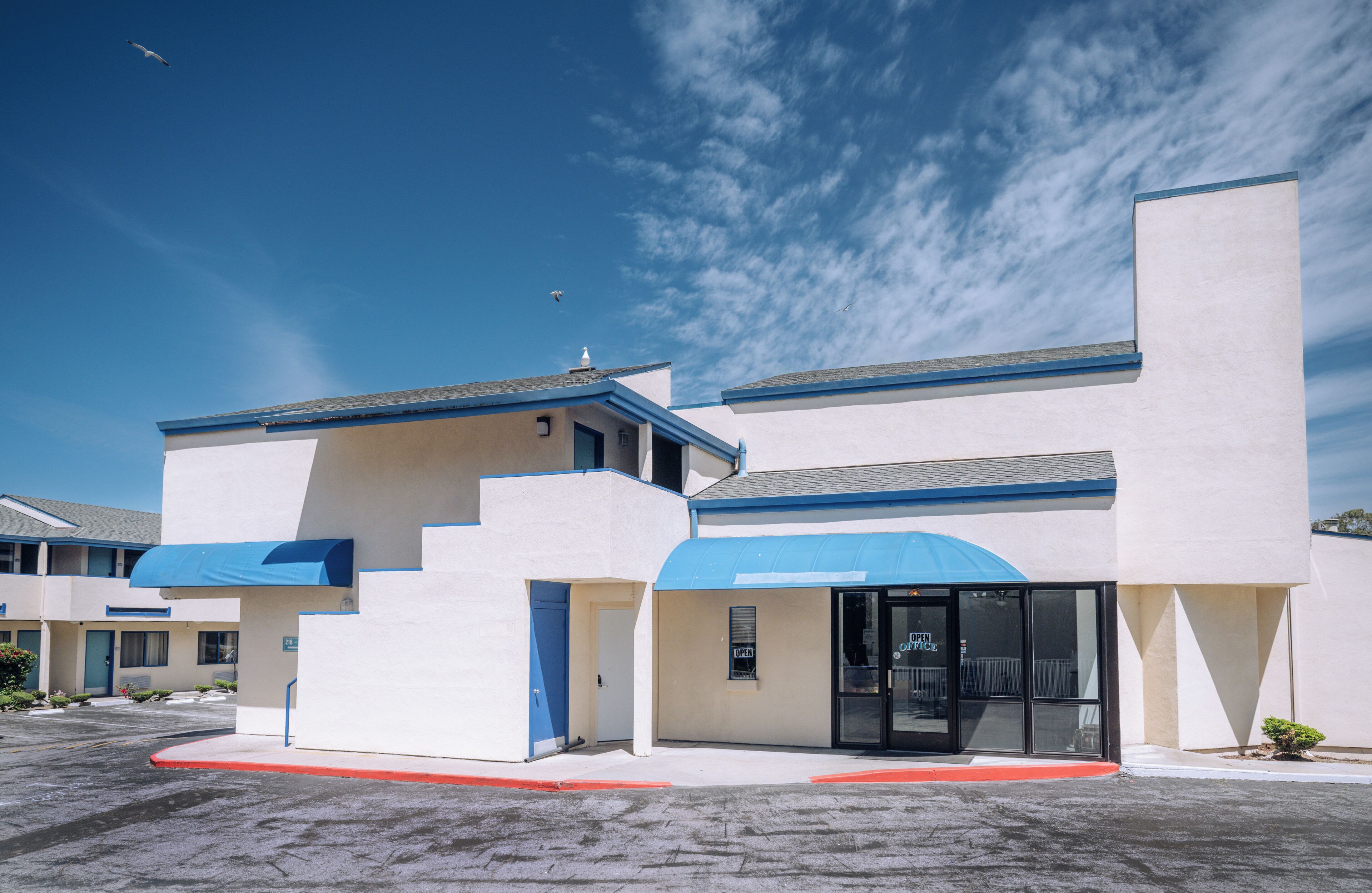 Un hotel moderno con tetto piatto, tenda parasole blu e cielo sereno.